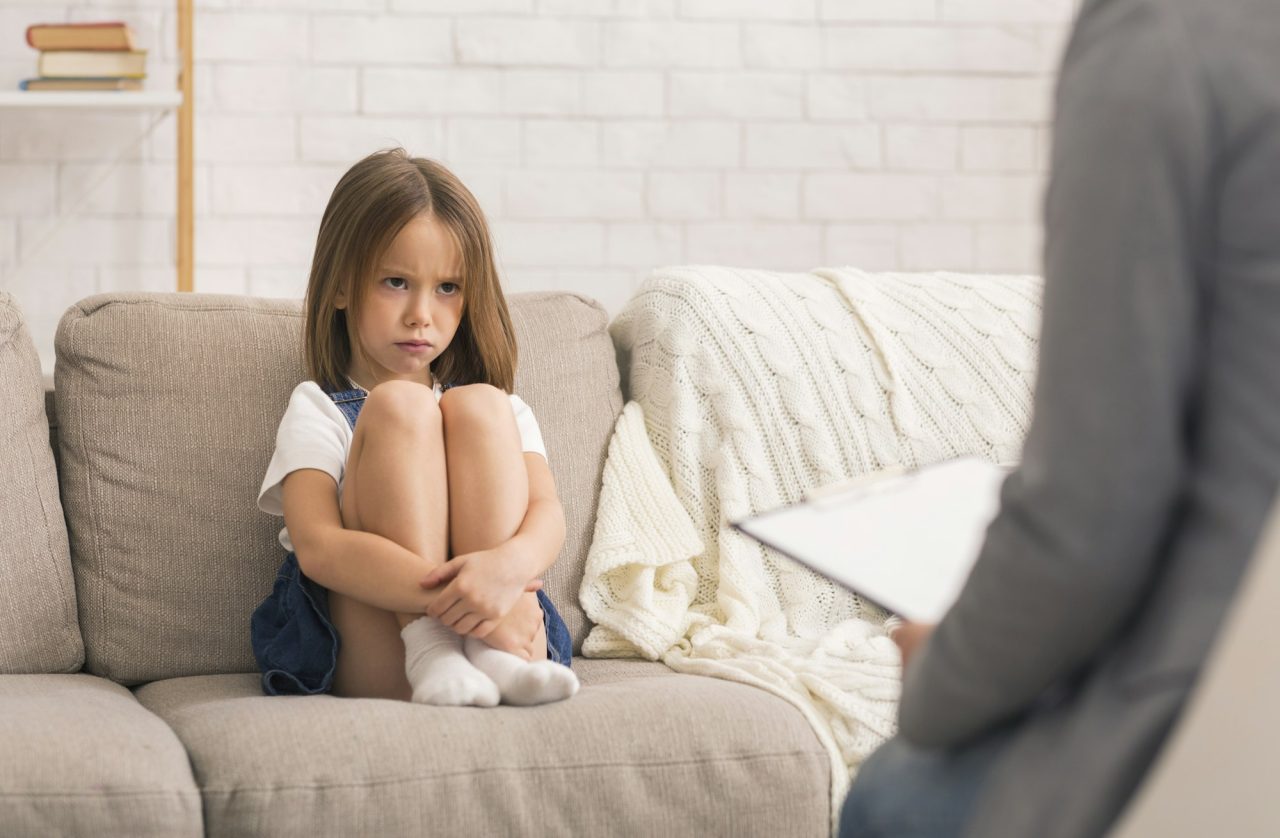 Concerned Little Girl Sitting Alone At Therapy Session With Children Psychologist